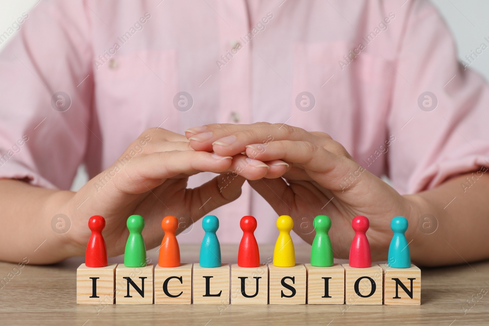 Photo of Woman protecting colorful pawns and wooden cubes with word Inclusion at table, closeup