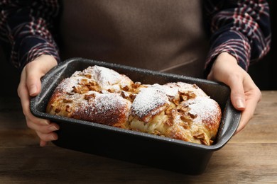 Woman holding baking pan with delicious yeast dough cake at wooden table, closeup