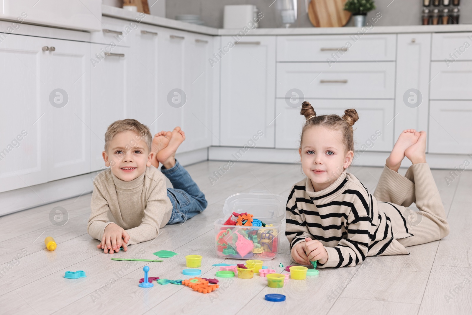 Photo of Cute little children playing together on warm floor in kitchen. Heating system