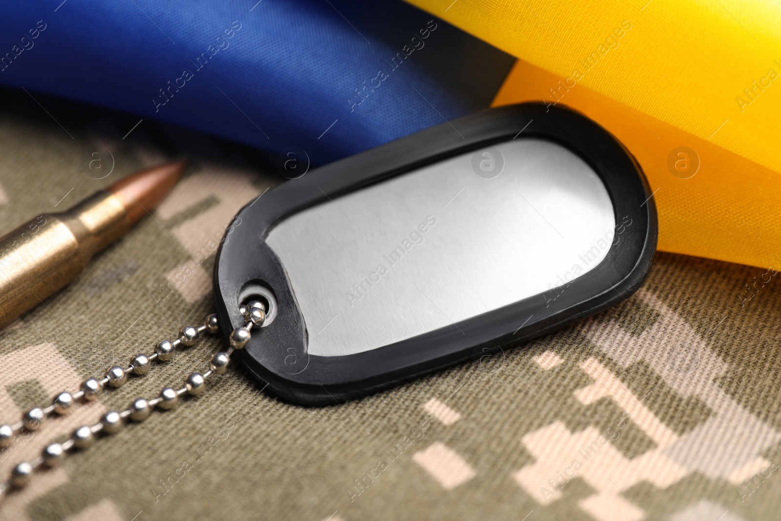 Photo of Military ID tag, bullet and Ukrainian flag on pixel camouflage, closeup