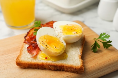 Photo of Toast with soft boiled egg and bacon on wooden board, closeup