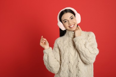 Photo of Beautiful young woman wearing earmuffs on red background. Space for text