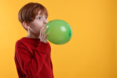 Photo of Boy inflating green balloon on orange background, space for text