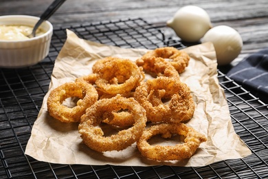 Cooling rack with homemade crunchy fried onion rings and sauce on wooden background