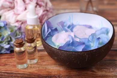 Photo of Spa composition. Aromatic water in bowl, bottles of essential oil and flowers on wooden table, closeup