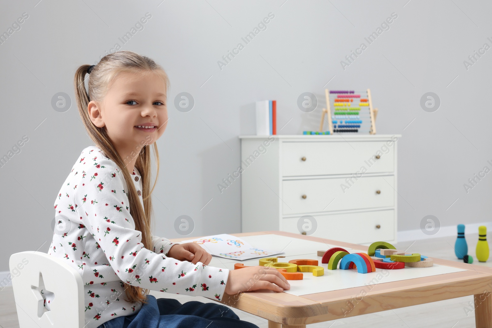 Photo of Motor skills development. Happy girl with colorful wooden arcs at white table in kindergarten