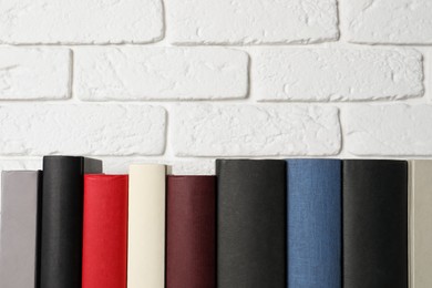 Photo of Many different hardcover books near white brick wall, space for text