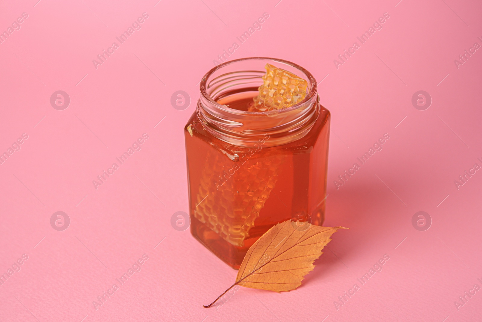 Photo of Jar with honey and autumn leaf on pink background