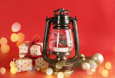 Beautiful Christmas snow globe in vintage lantern, gift boxes and decor on red background, bokeh effect