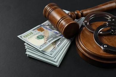 Photo of Judge's gavel, money and handcuffs on black background, closeup