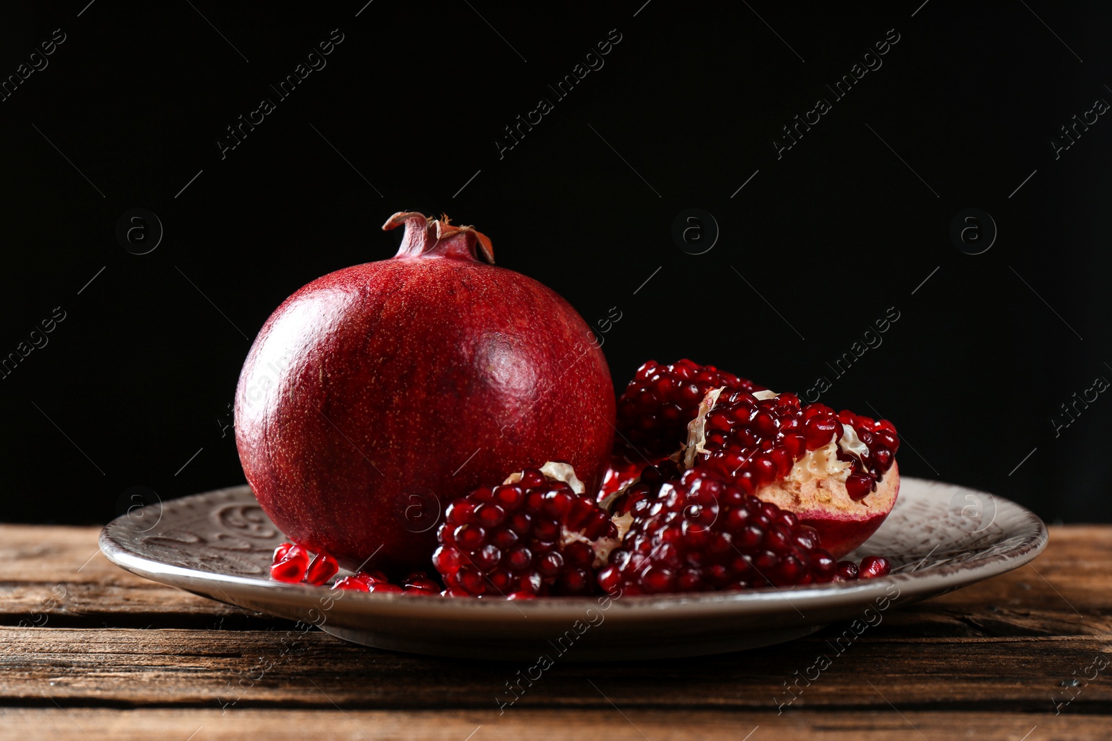 Photo of Plate with ripe pomegranates on table against black background