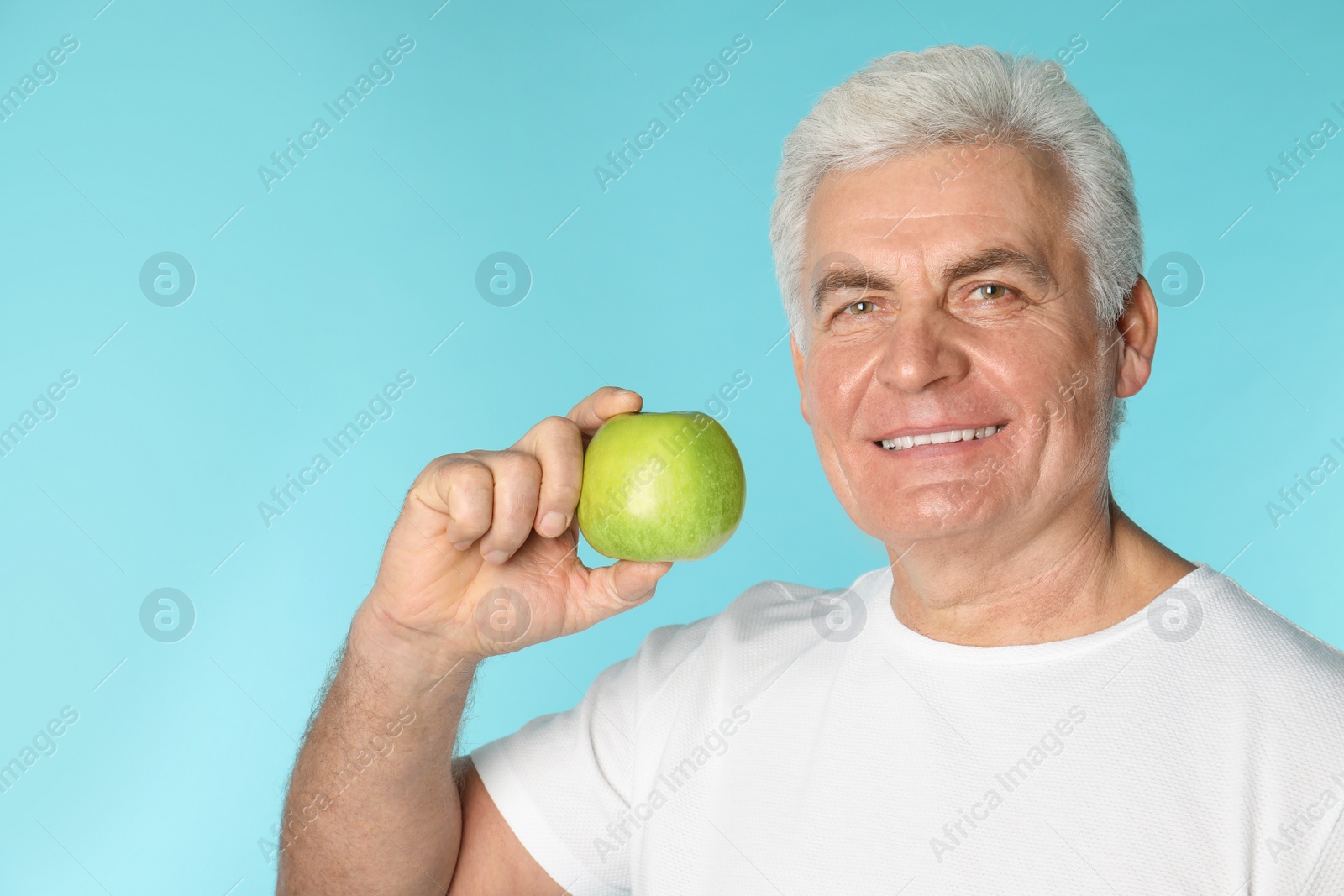 Photo of Mature man with healthy teeth holding apple on color background. Space for text