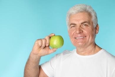 Photo of Mature man with healthy teeth holding apple on color background. Space for text