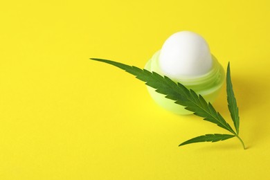 Photo of Hemp lip balm and green leaf on yellow background, space for text. Natural cosmetics