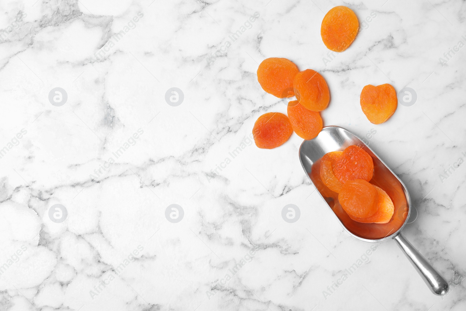 Photo of Scoop of apricots on marble background, top view with space for text. Dried fruit as healthy food