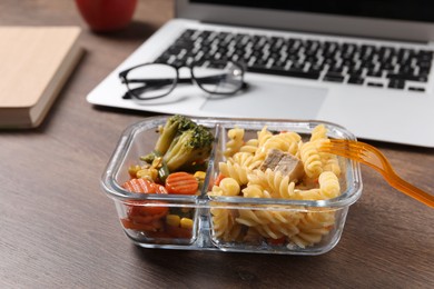 Photo of Container of tasty food, fork, laptop and glasses on wooden table. Business lunch