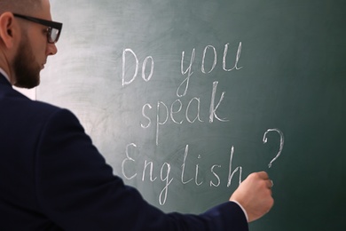 Teacher writing words Do You Speak English? on green chalkboard, closeup