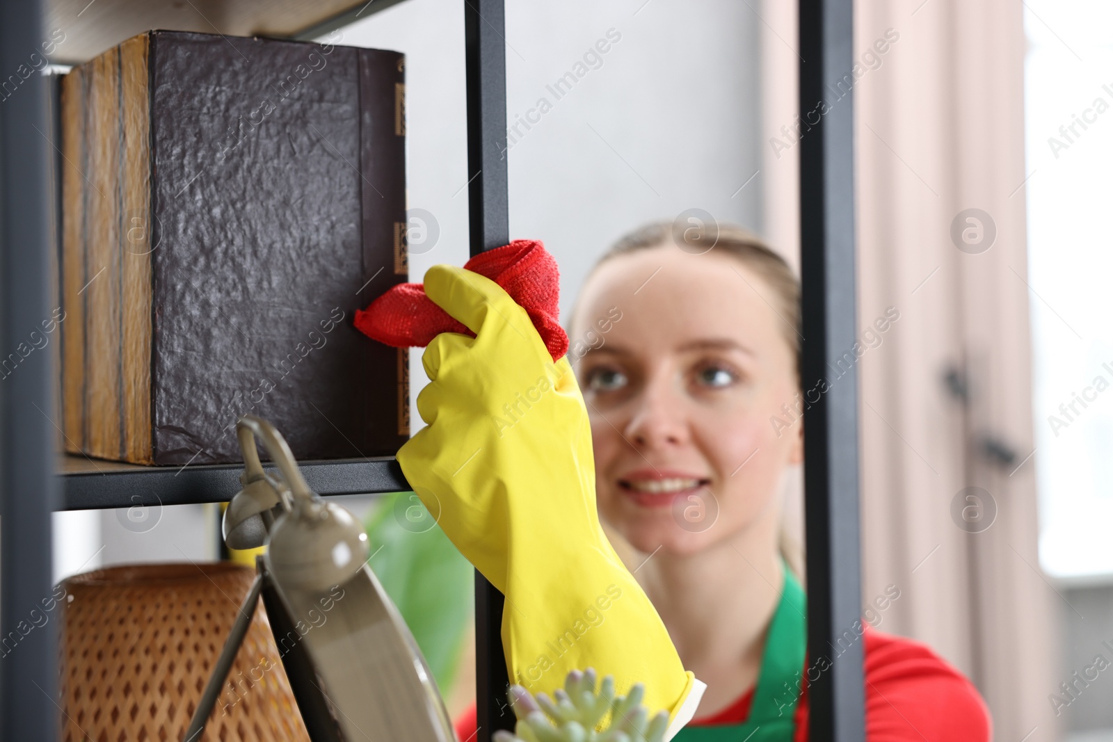 Photo of Woman cleaning shelving unit with rag at home, selective focus