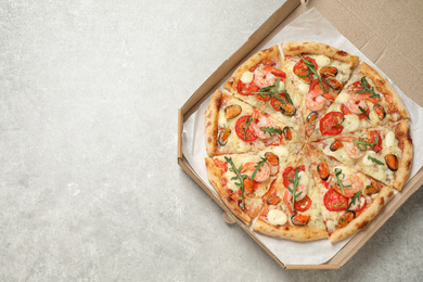 Photo of Delicious seafood pizza in box on light grey table, top view. Space for text
