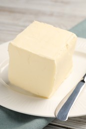 Block of tasty butter and knife on white wooden table, closeup