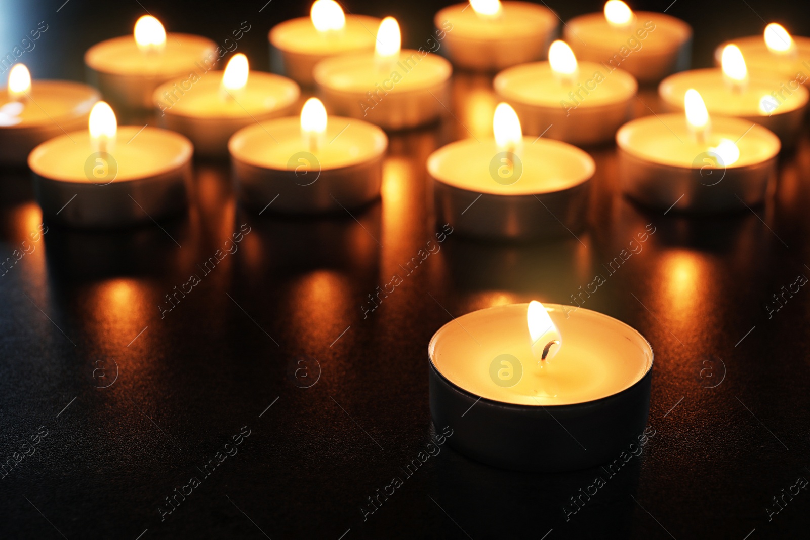 Photo of Wax candles burning on table in darkness, closeup