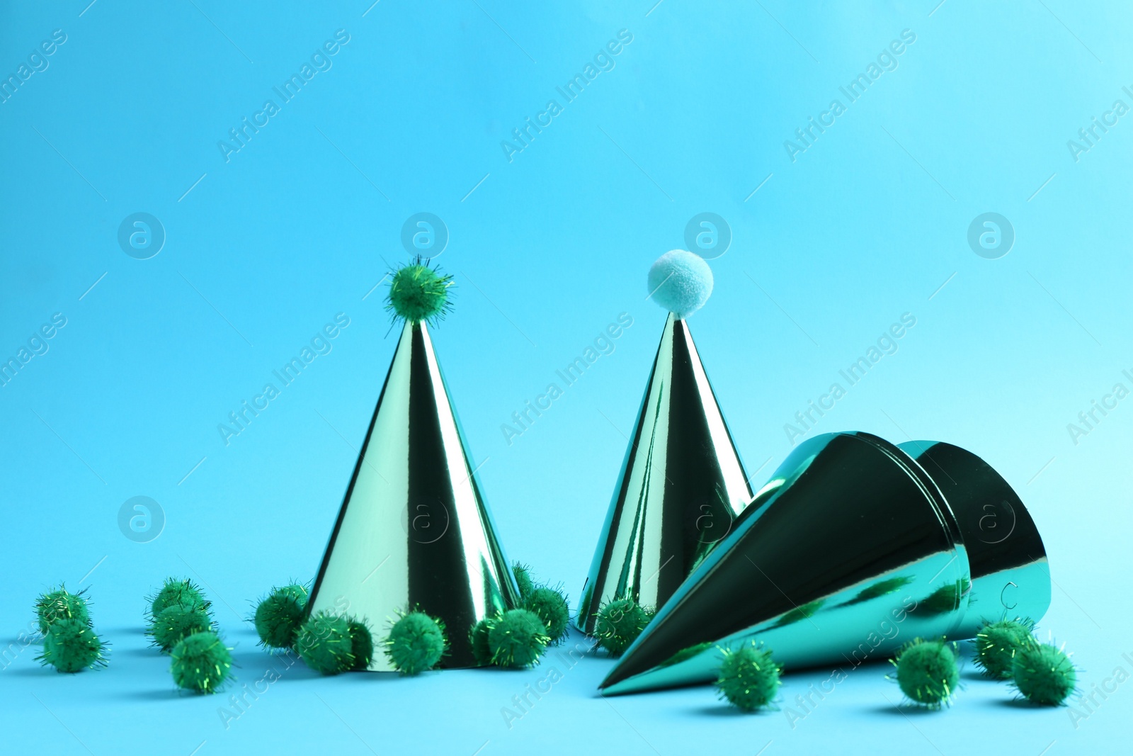 Photo of Party hats with green pompoms on light blue background