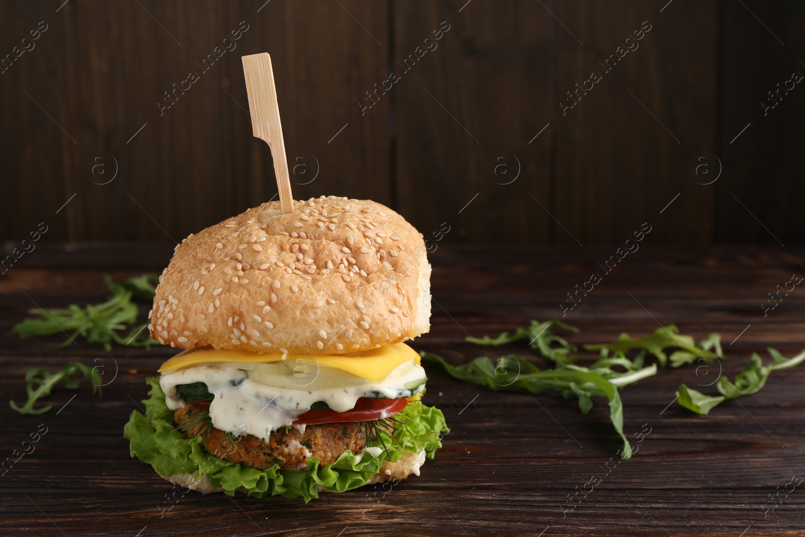 Photo of Delicious vegetarian burger and arugula on wooden table