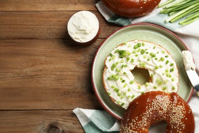 Photo of Delicious bagel with cream cheese and green onion on wooden table, flat lay. Space for text