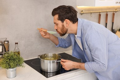 Photo of Man tasting delicious chicken soup in kitchen