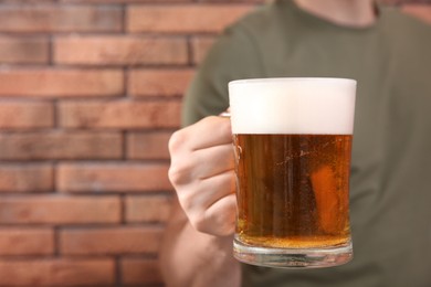 Man with glass of tasty beer near red brick wall, closeup. Space for text