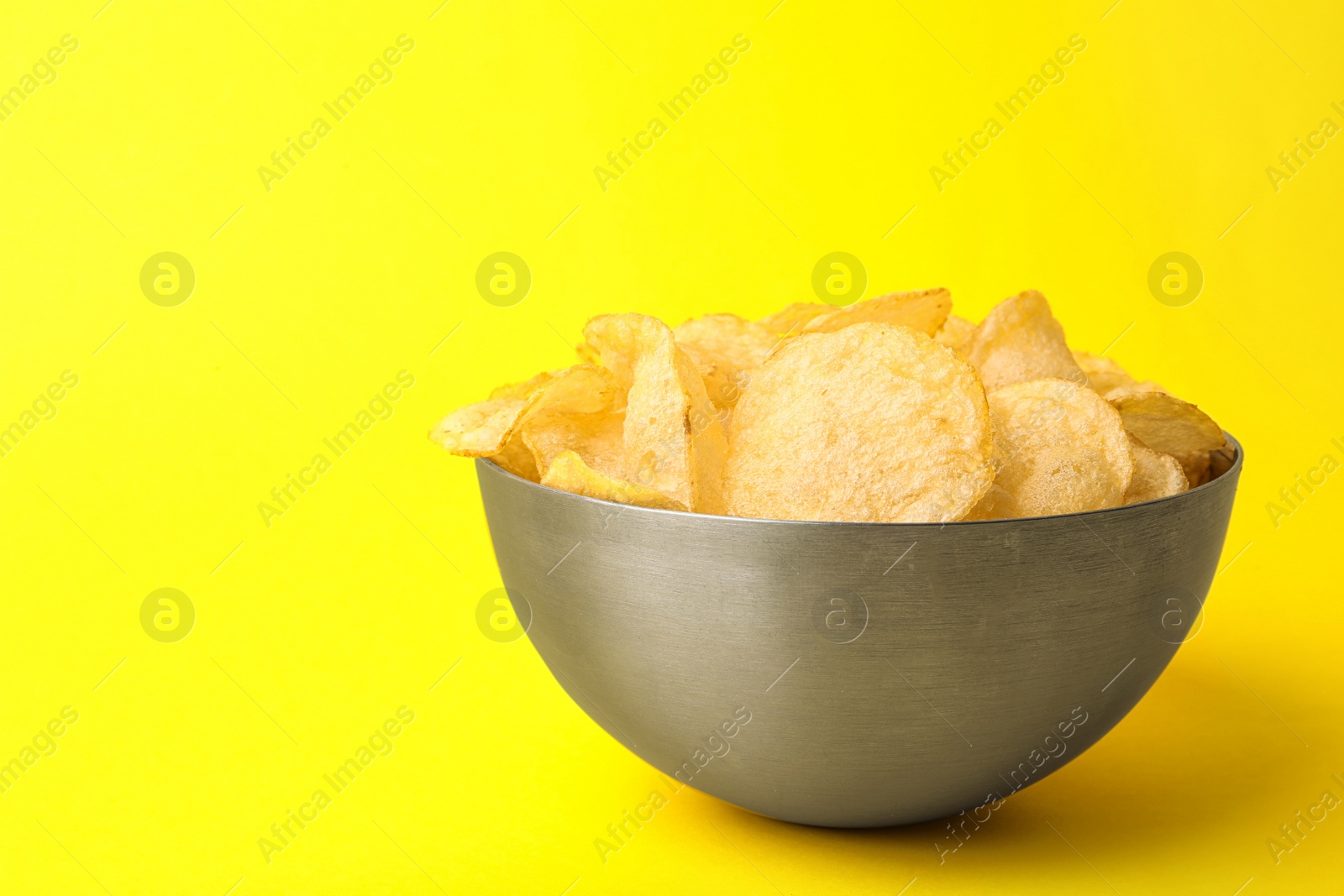 Photo of Delicious crispy potato chips in bowl on color background, space for text