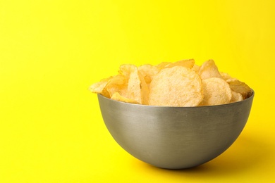 Delicious crispy potato chips in bowl on color background, space for text