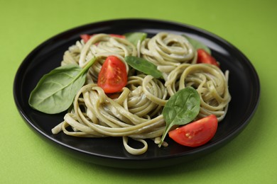 Photo of Tasty pasta with spinach, sauce and tomatoes on green table, closeup