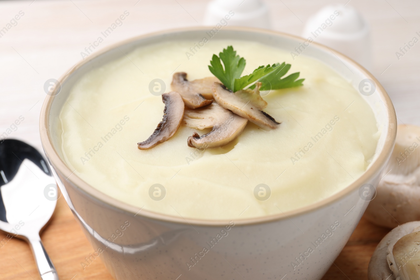 Photo of Bowl of tasty cream soup with mushrooms, parsley and spoon on table, closeup