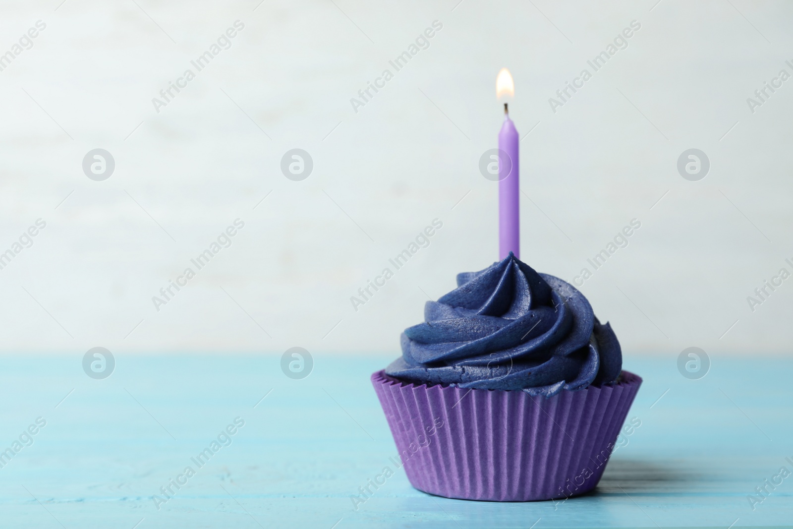 Photo of Delicious birthday cupcake with cream and burning candle on blue wooden table. Space for text