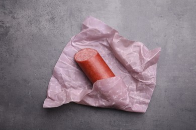Photo of Fresh tasty sausage in beeswax food wrap on grey table, top view