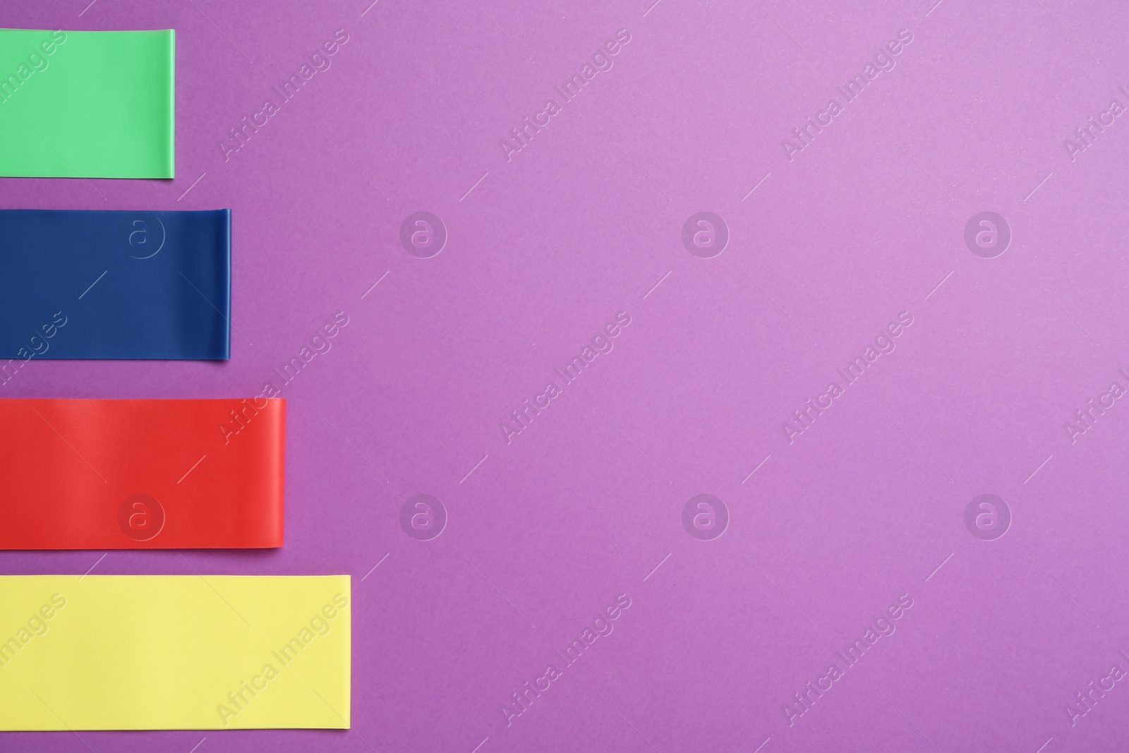 Photo of Set of fitness elastic bands on purple background, flat lay. Space for text