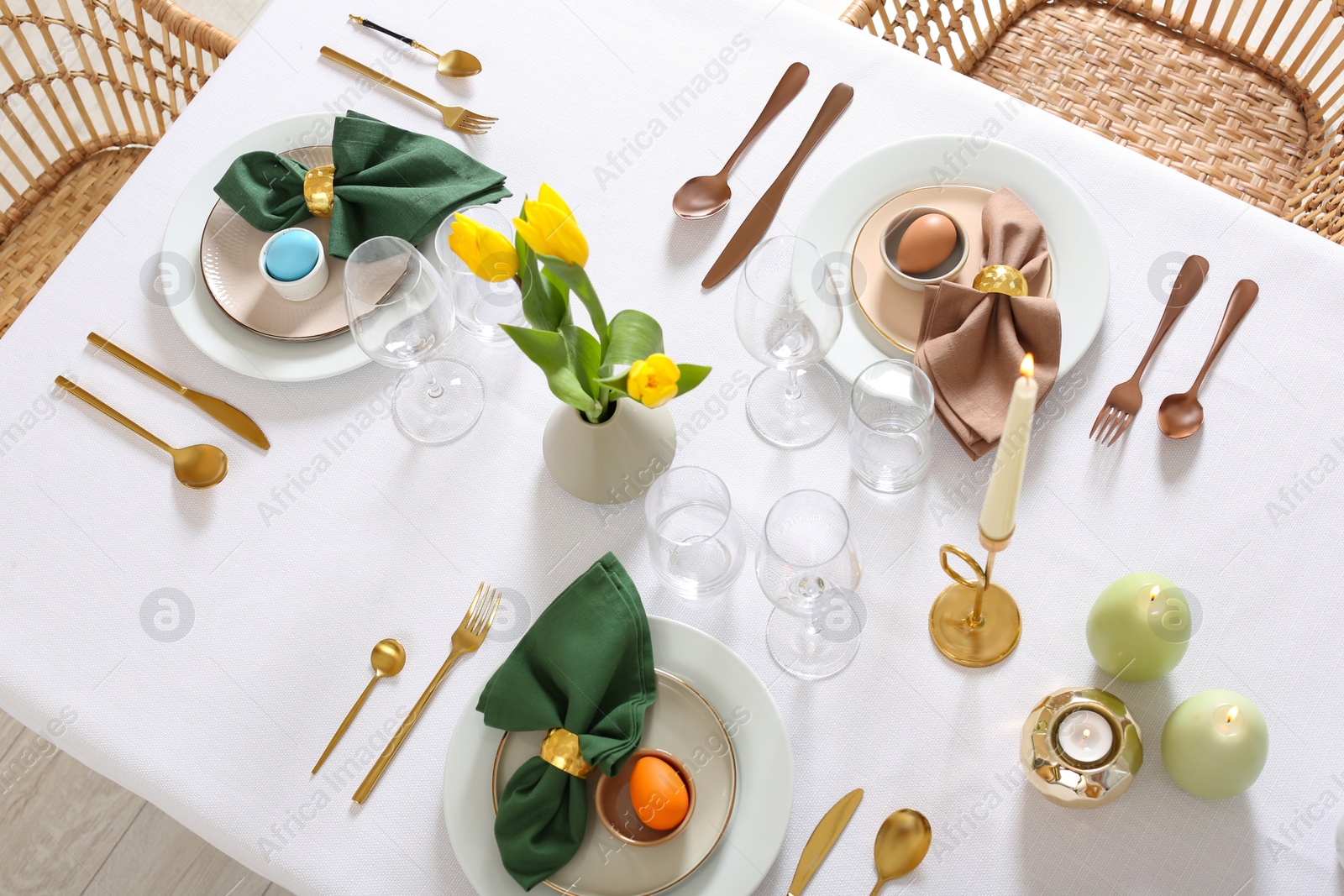 Photo of Festive Easter table setting with painted eggs, burning candles and yellow tulips, view from above