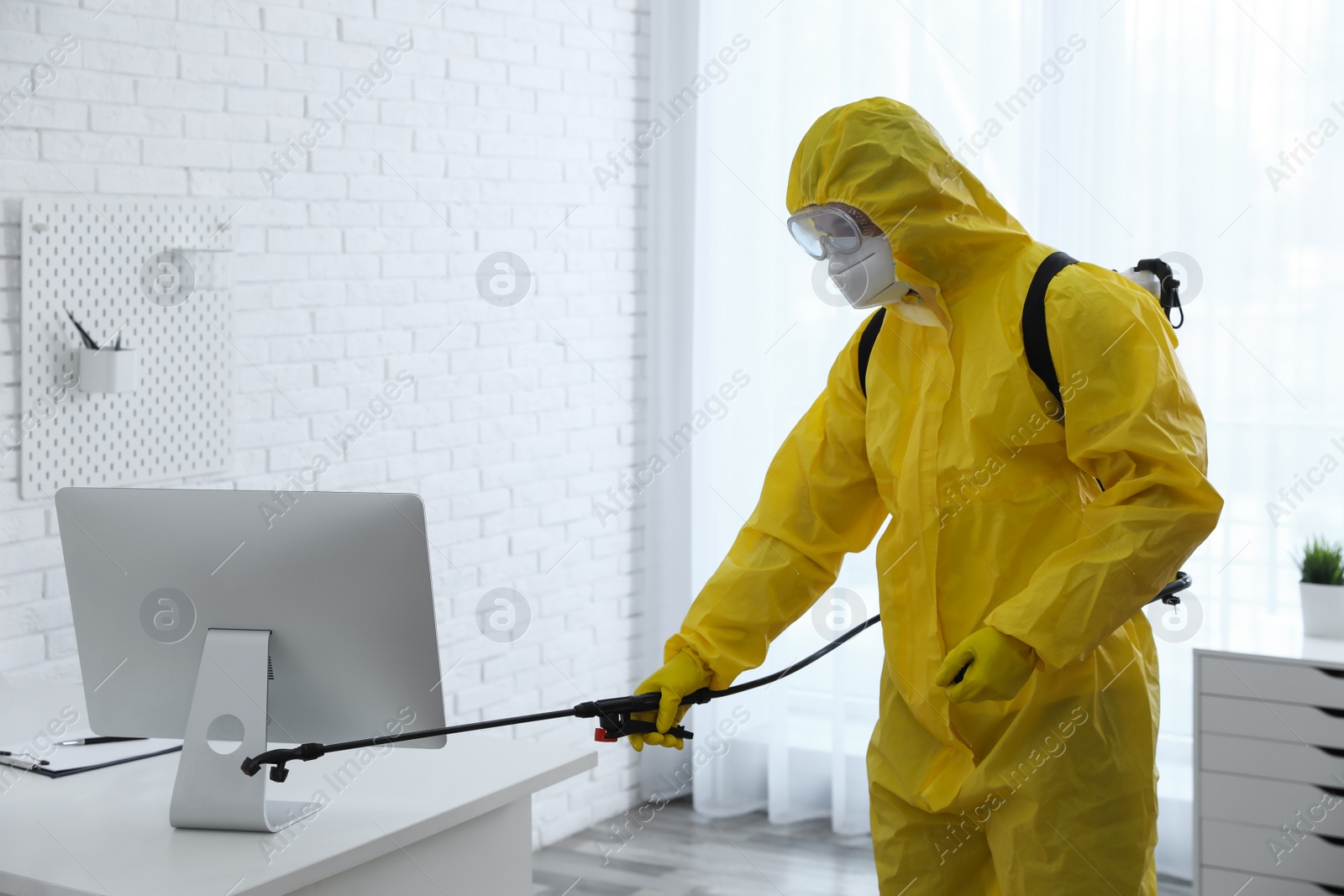 Photo of Employee in protective suit sanitizing office. Medical disinfection