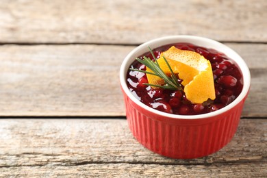 Photo of Fresh cranberry sauce in bowl, rosemary and orange peel on wooden table, closeup. Space for text