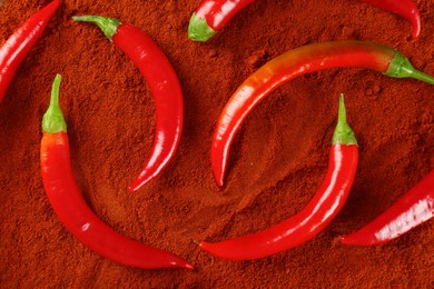 Photo of Fresh chili peppers on paprika powder, flat lay