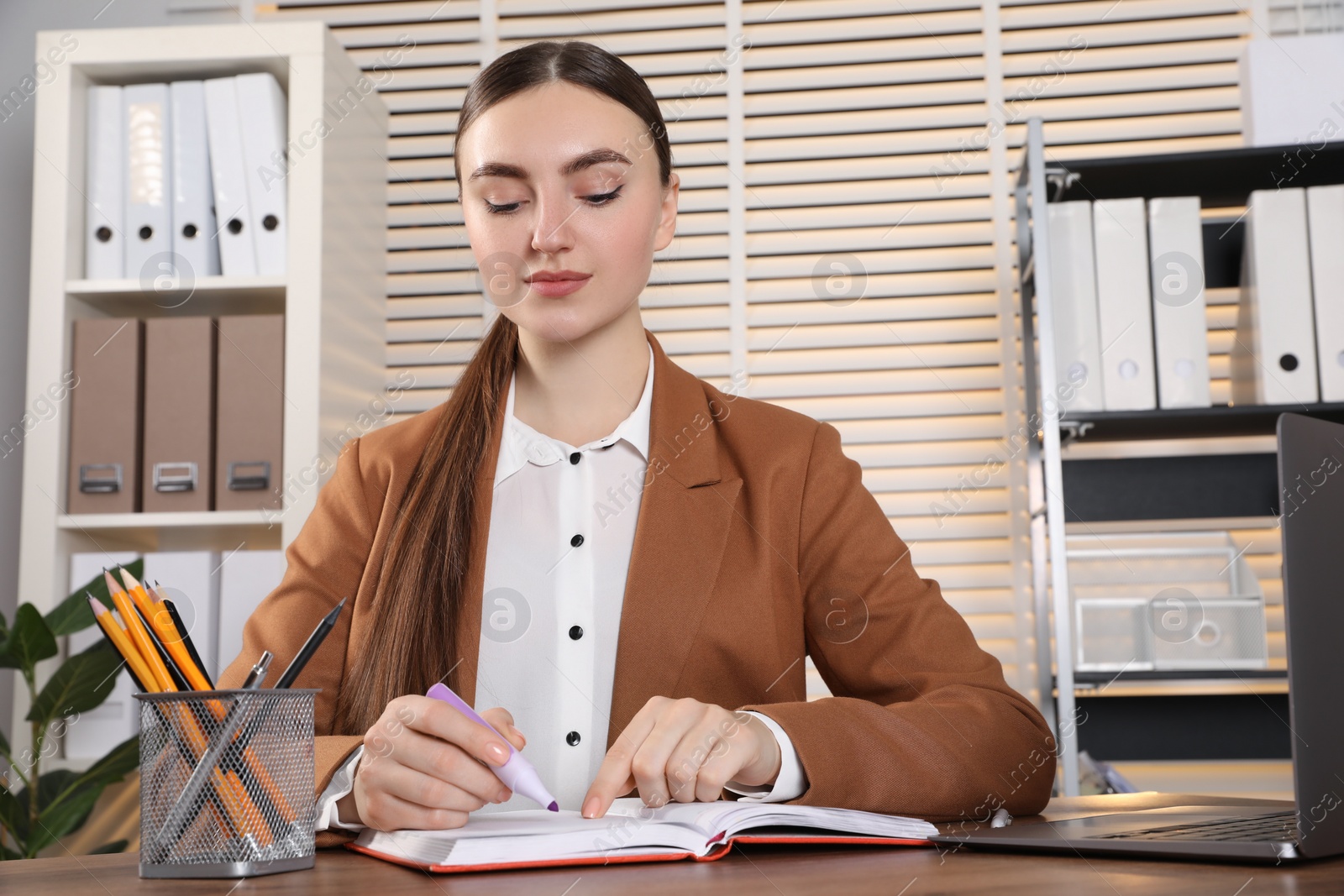 Photo of Woman taking notes at wooden table in office