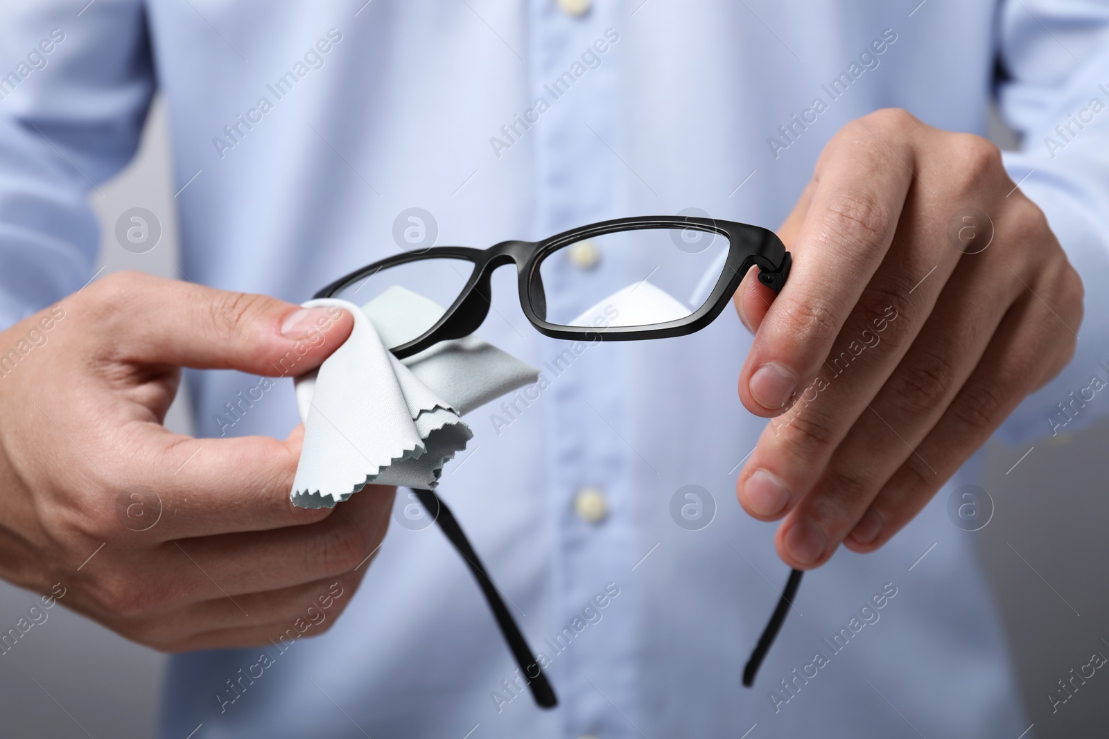 Photo of Man wiping glasses with microfiber cloth on light grey background, selective focus