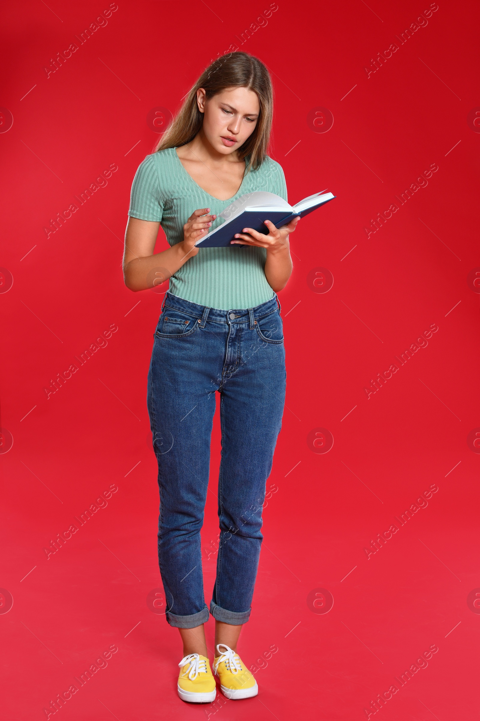 Photo of Beautiful young woman reading book on red background