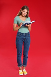 Beautiful young woman reading book on red background