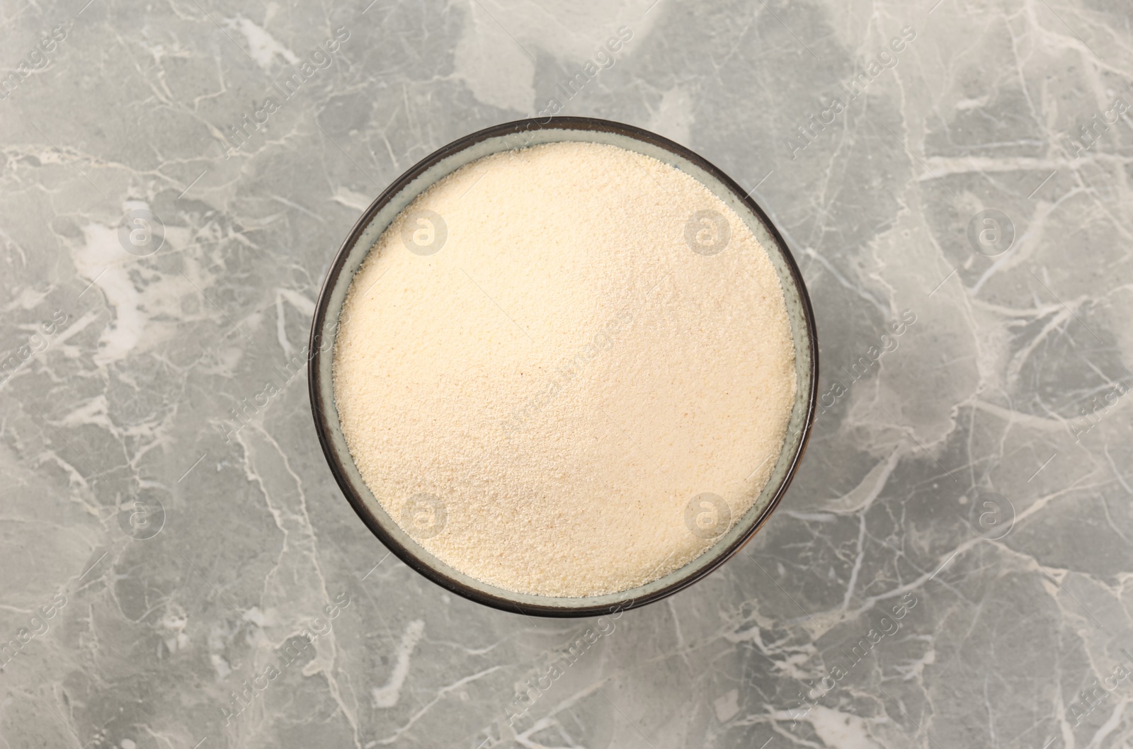 Photo of Uncooked organic semolina in bowl on grey table, top view