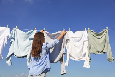 Photo of Woman hanging clothes with clothespins on washing line for drying against blue sky, back view