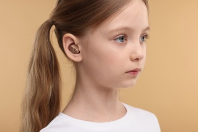 Photo of Little girl with hearing aid on pale brown background, closeup