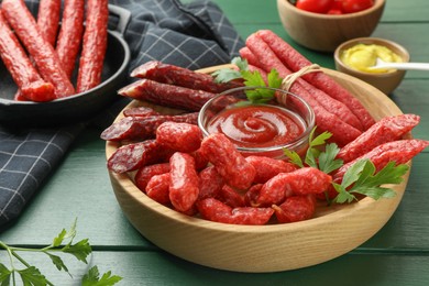 Different thin dry smoked sausages, parsley and sauces on green wooden table