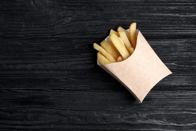 Delicious french fries in paper box on black wooden table, top view. Space for text